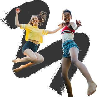 Two young women joyfully jump against a black background. One wears a yellow top, the other a striped one. Both are barefoot, conveying energy and freedom.