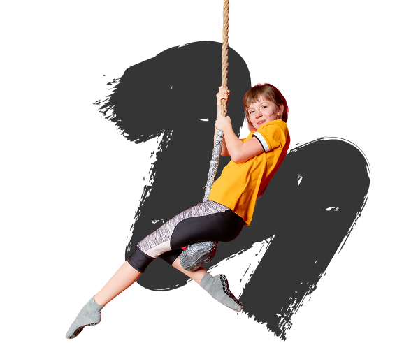 Child in a yellow shirt and black leggings joyfully swinging on a rope against a black background. The expression conveys excitement and playfulness.